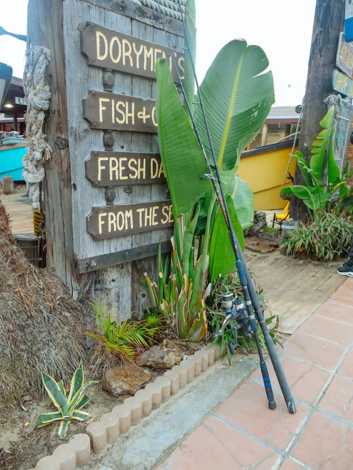 Fishing rods lean against a rustic sign at an outdoor fish market, exuding charm.